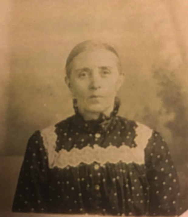 a woman with hair scraped back is wearing a frilly dress with lace and a high collar.