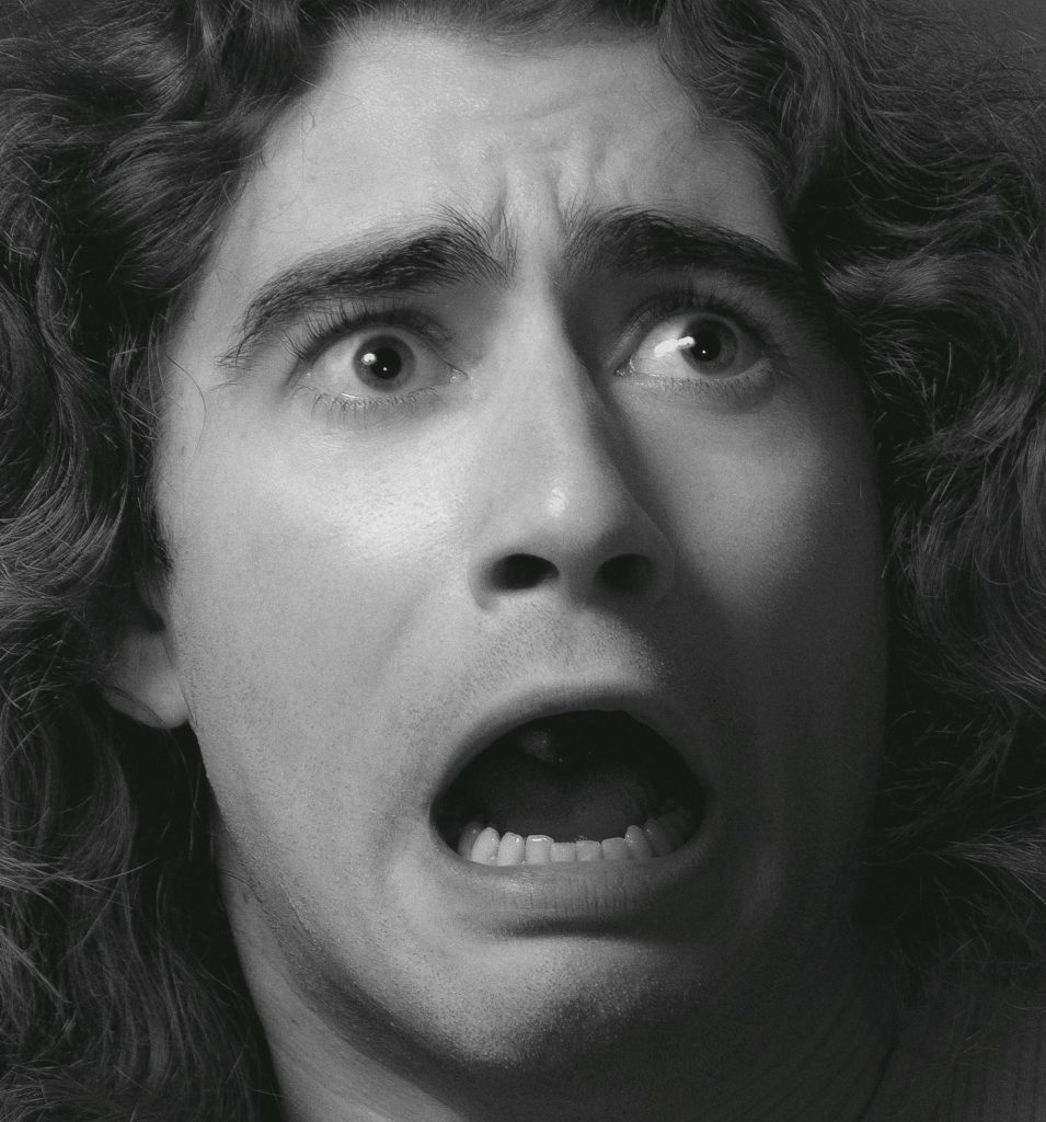 A white man with curly hair with a shocked expression.