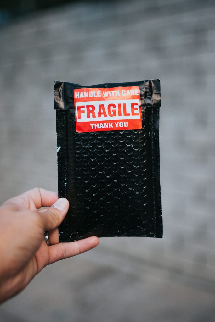 A hand holding a small, black package that has Handle with care, fragile, thank you, on a sticker on it.